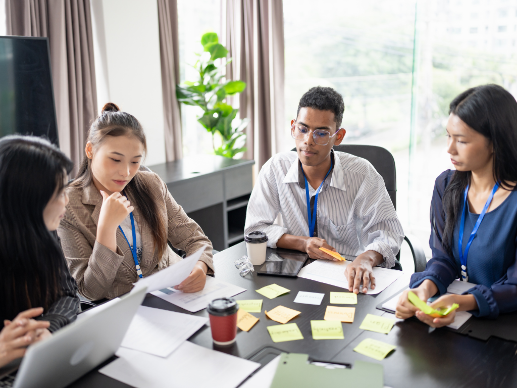 A group of four professionals meeting around a table with sticky notes and laptops.